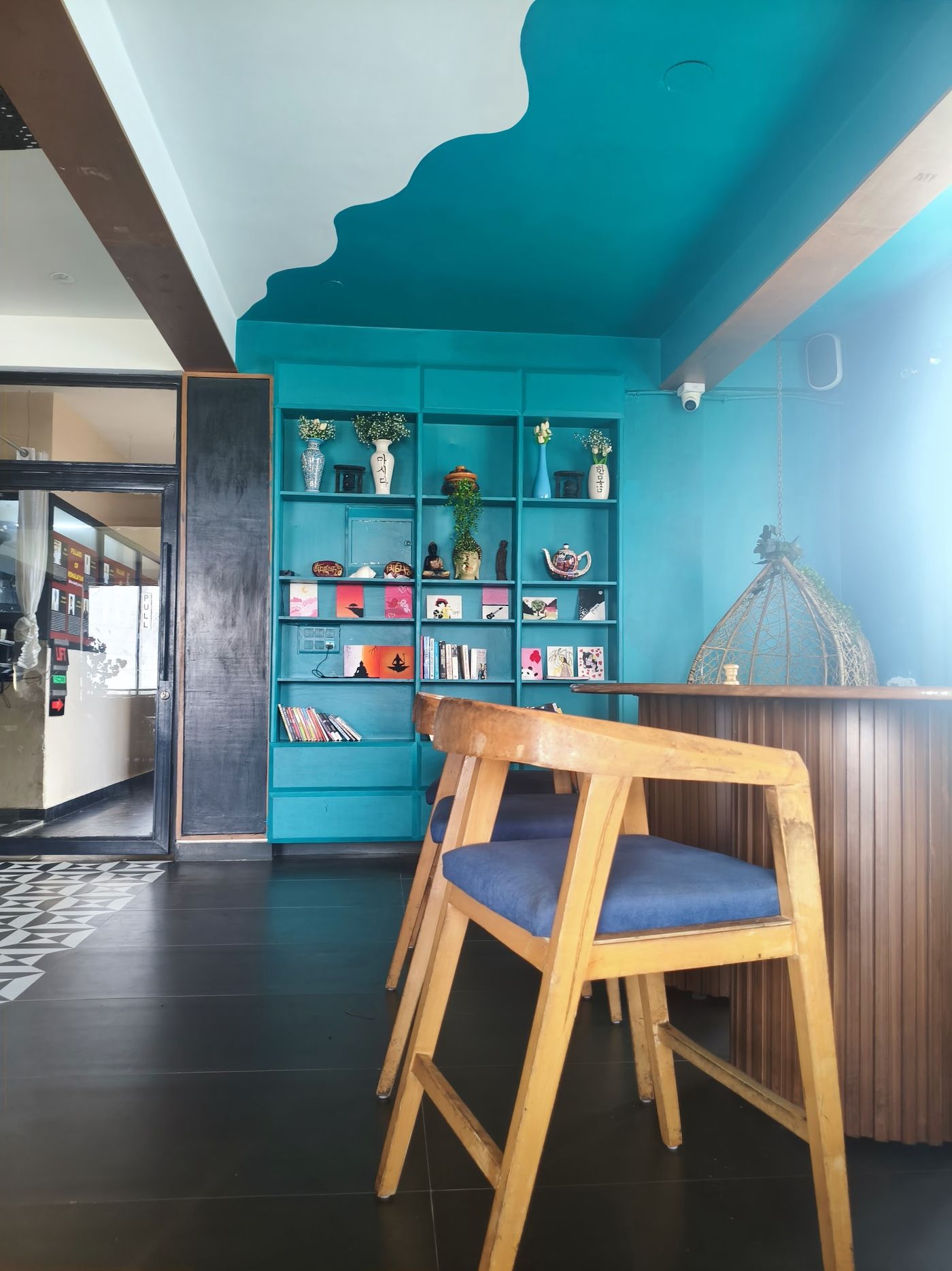 The café corner with a teal wall, bookshelves and wooden bar stools
