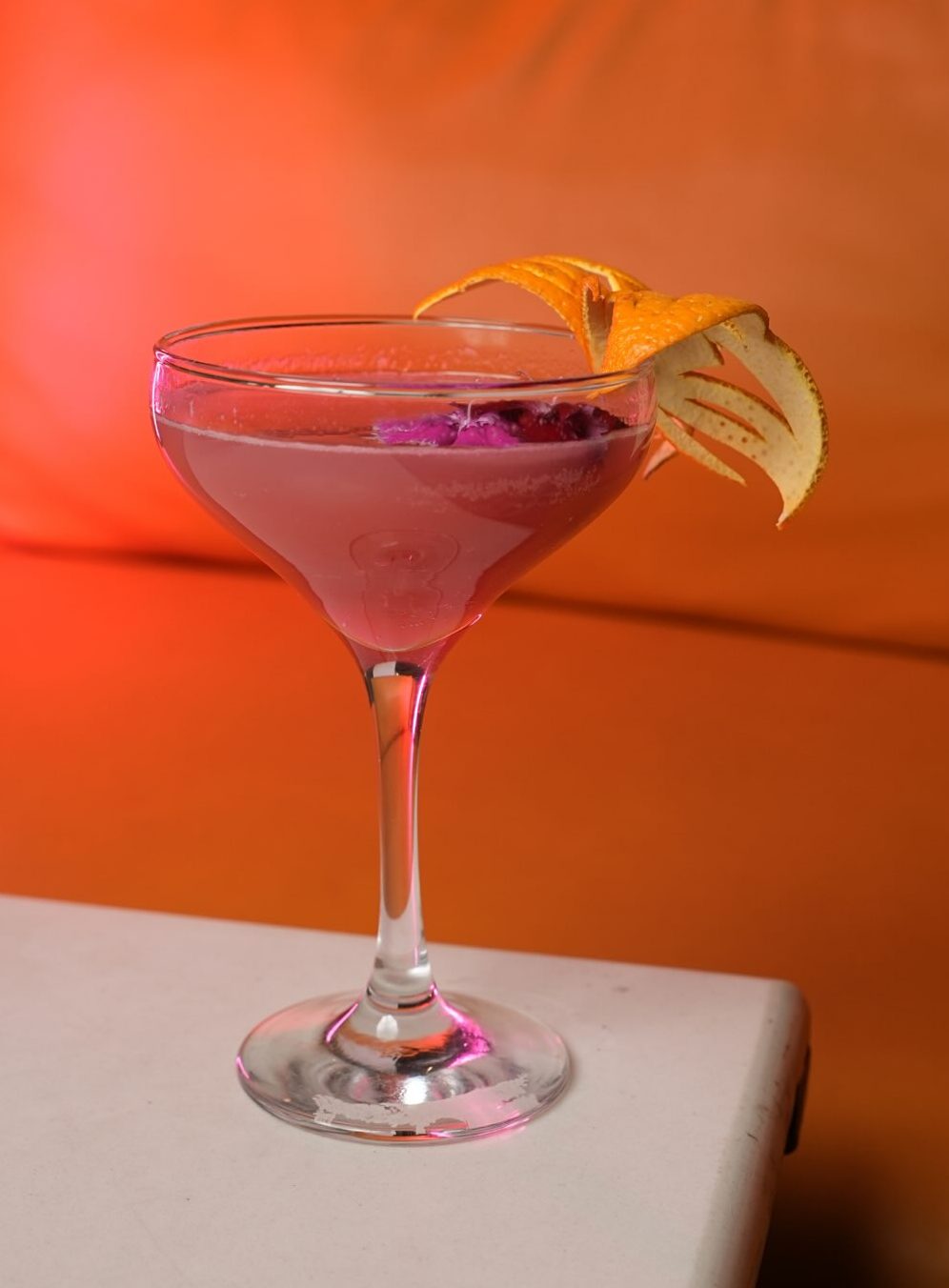 Pink drink in a coupe glass garnished with orange peel